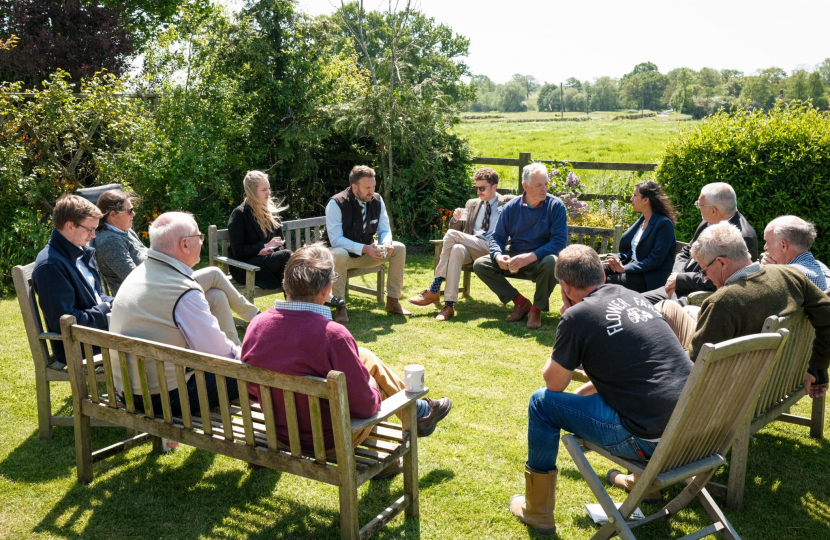 Claire is sitting with farmers in a circle in a green field.