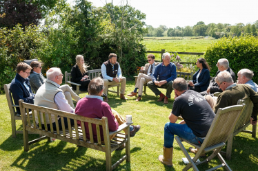 Claire is sitting with farmers in a circle in a green field.