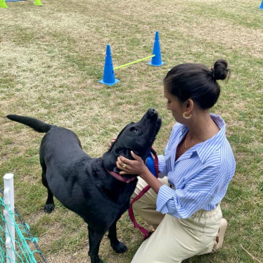 Claire is kneeling down stroking Eric, a black labrador.