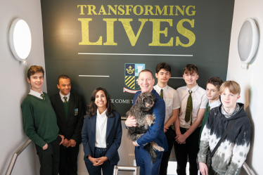 Claire is standing in the stairwell of Sunnydown School with Mr Jensen and students. Mr Jensen is holding a dog.