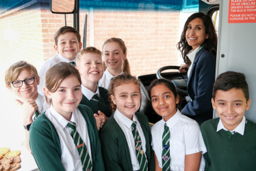 Claire is sitting in the driver's seat of the bus, with children from Meath Green Junior School smiling in front of her.